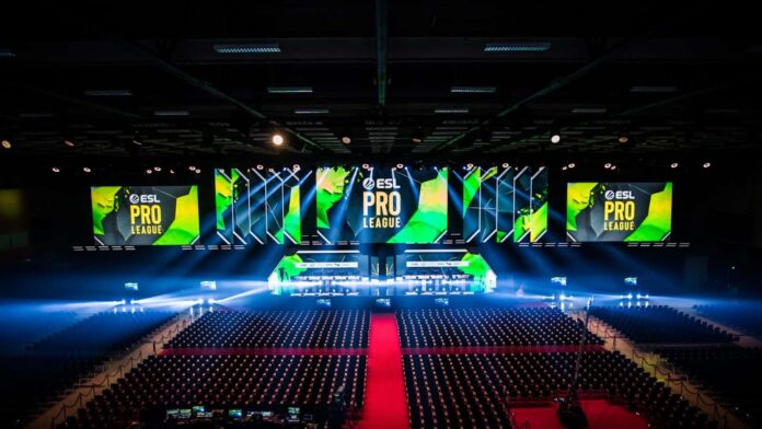 An empty arena venue is lit up with spotlights and monitors above the stage are lit in green with the words "ESL Pro League" on them.