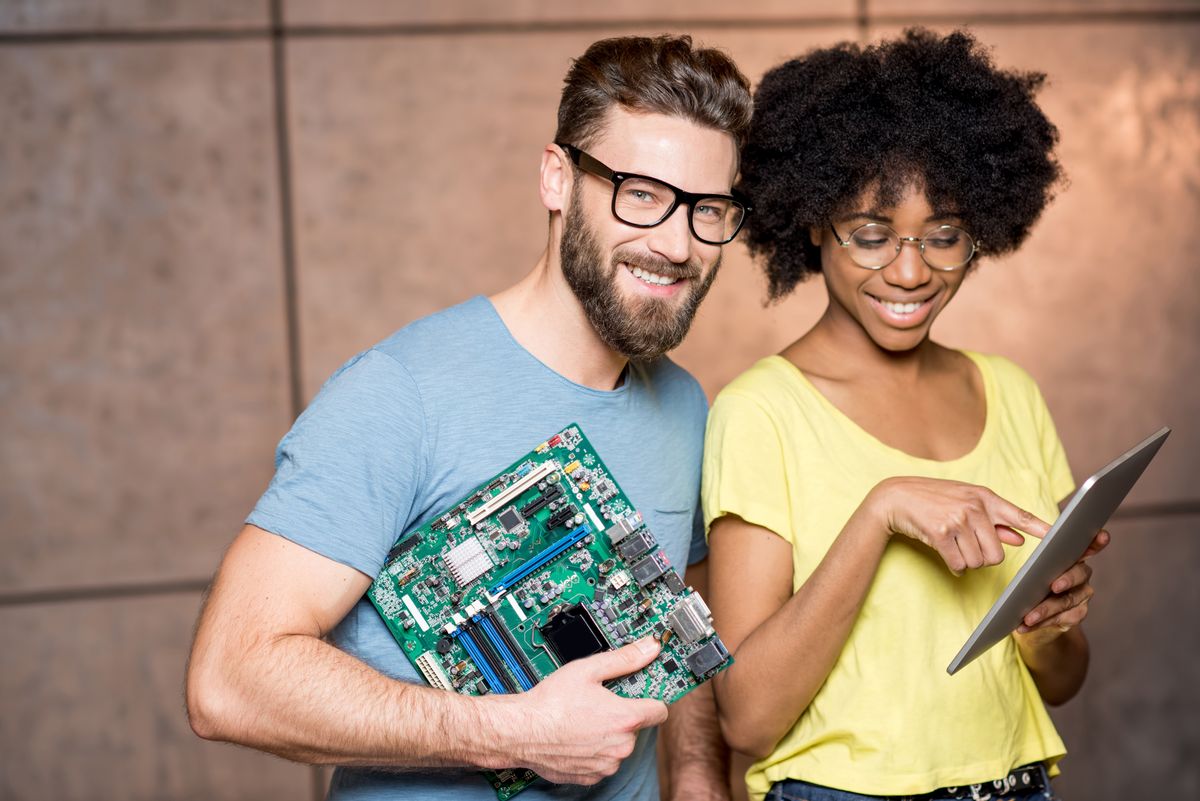 Multi ethnic programmers dressed casually standing together with computer motherboard and digital tablet on the wall background indoors