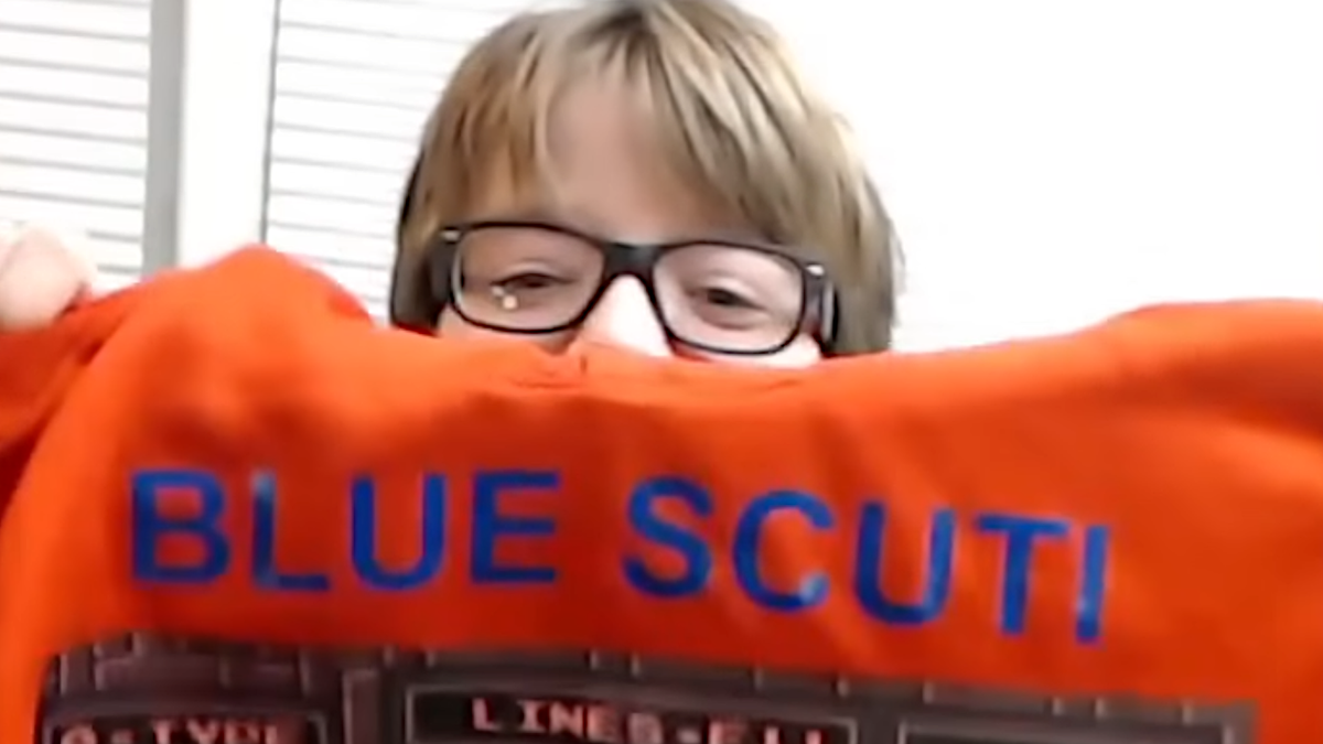 Blue Scuti holds up an orange hoodie with the words