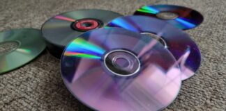A collection of upturned CDs, DVDs and Blu-rays on a carpeted floor