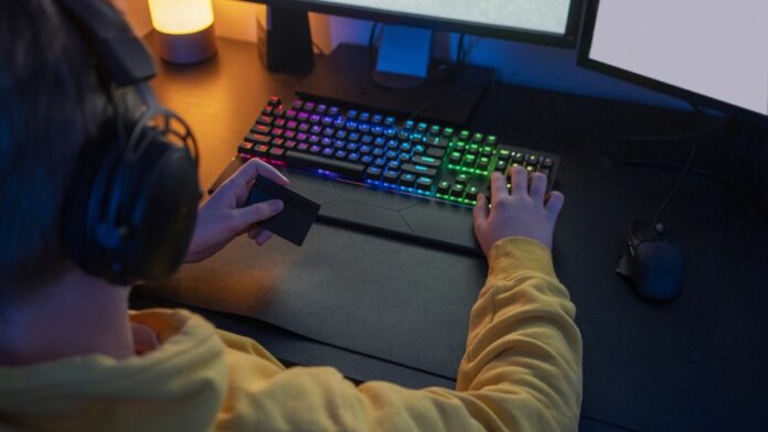 A boy holding is credit card while playing a PC game.