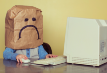 A child with a sad paper bag on their head sits staring at an old PC.